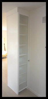 White floor-to-ceiling bookcase back side of entertainment center with 1/4'' glass paneled door.