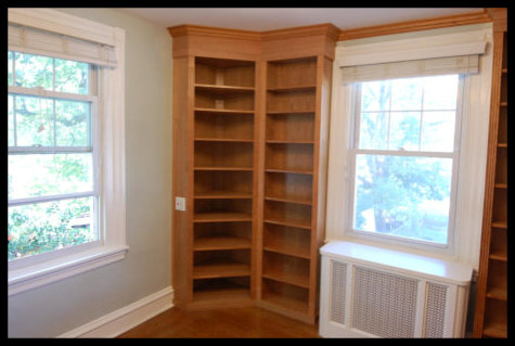 Double-wide 45 degree cherry corner bookcase; floor-to-ceiling open-face shelving with custom crown molding.
